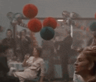 a blurry picture of a group of people sitting at a table with balloons hanging from the ceiling .