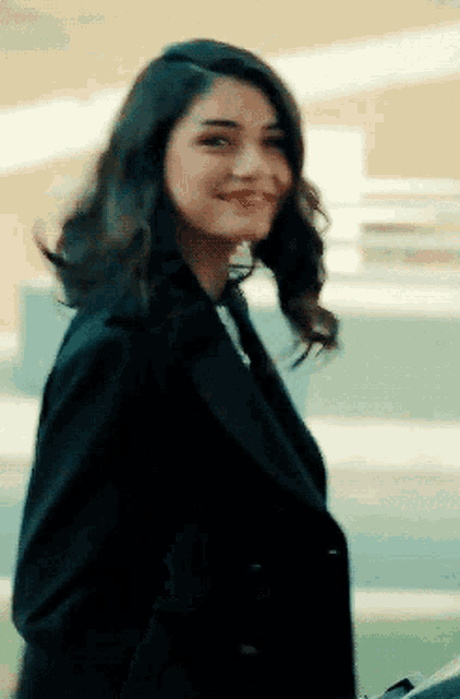a woman in a black coat smiles and looks at the camera