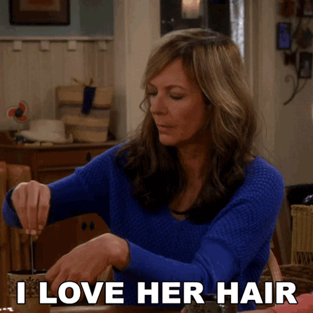 a woman in a blue sweater is sitting at a table with the words i love her hair above her