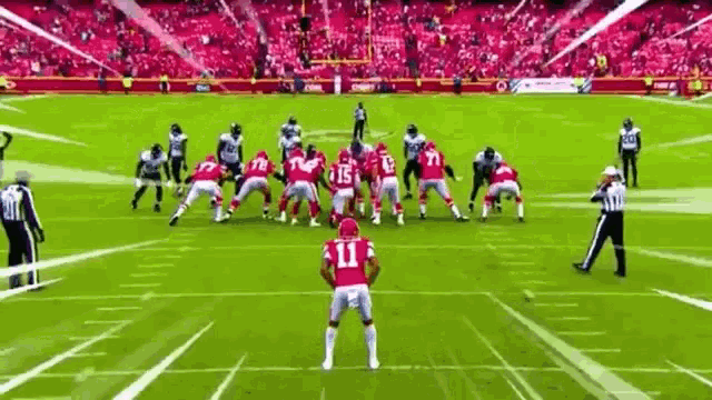 a group of football players are playing a game on a field with a referee in the foreground .