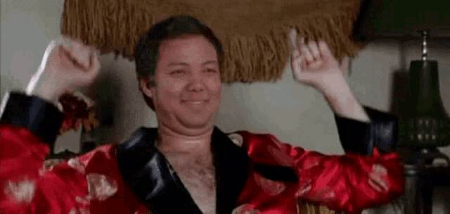 a man in a red robe is sitting in a living room with his arms in the air .