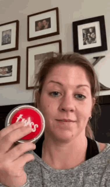a woman is holding a can of twizzlers in front of a wall of framed pictures