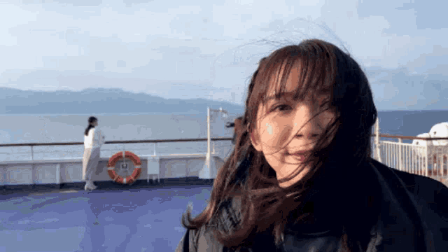 a woman with her hair blowing in the wind is standing on a boat