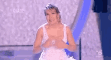 a woman in a white dress is making a heart with her hands on a stage .