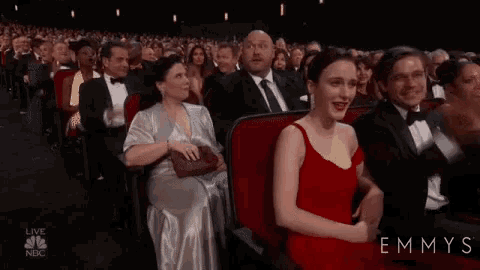 a woman in a red dress is sitting next to a man in a suit in a crowd of people .