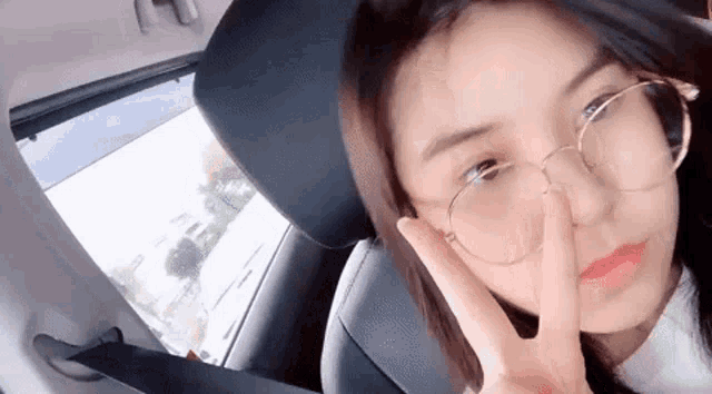 a woman wearing glasses is sitting in the back seat of a car and making a peace sign .