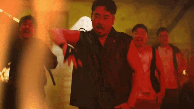 a group of men are standing in a dark room with red lights behind them