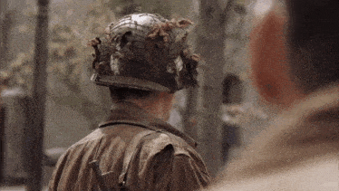 a man wearing a helmet and a brown jacket is talking to another man