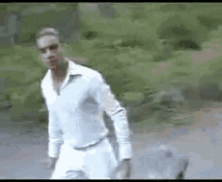 a man in a white shirt and white pants is walking with a dog .