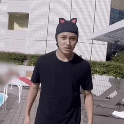 a young man wearing a black t-shirt and a cat hat is standing in front of a pool .