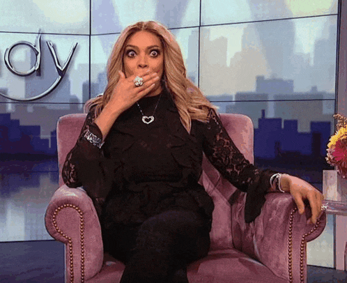 a woman is sitting in a chair with her hand over her mouth in front of a wall with the word city on it