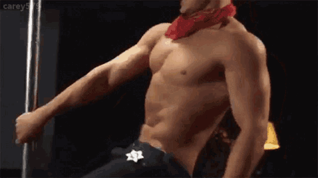 a shirtless man is dancing on a pole with a star on his belt .
