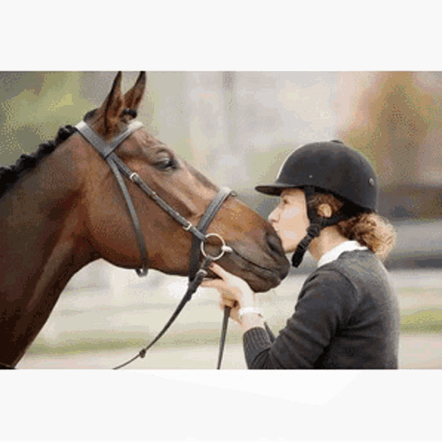 a woman wearing a helmet kisses a brown horse on the nose .