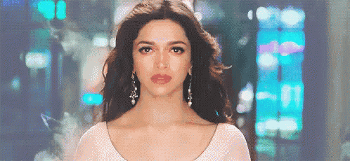 a woman in a white dress and earrings is standing in front of a blurry background and looking at the camera .