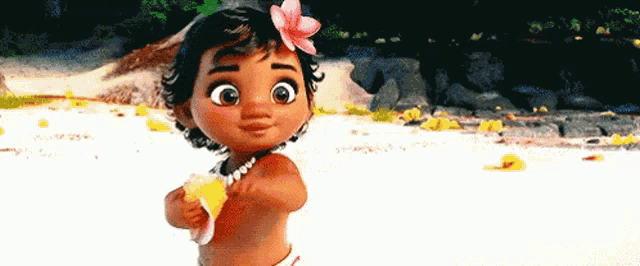 a baby girl with a flower in her hair is standing on a beach holding a shell .