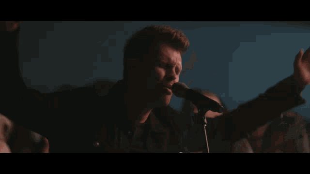 a man singing into a microphone in front of a crowd with their hands in the air
