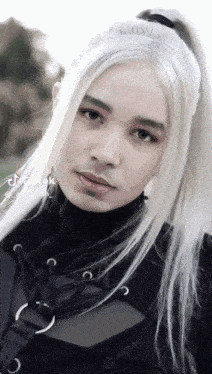 a young man with long white hair is wearing a black top and a black vest .