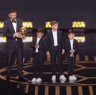 a man in a tuxedo is holding a trophy while three young boys stand behind him