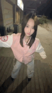 a young woman in a pink jacket is standing on a wooden floor .
