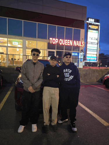 three men are posing for a picture in front of a building that says top queen nails