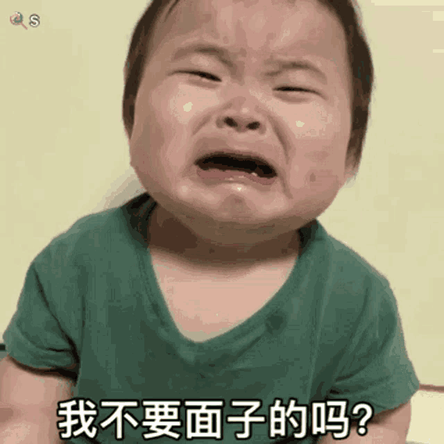 a baby in a green shirt is crying with chinese writing on his face