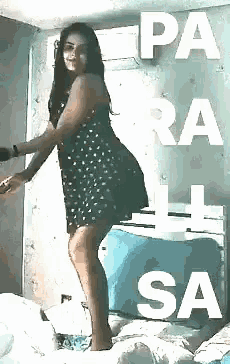 a woman in a polka dot dress is standing on a bed with the words pa ra sa written on the wall behind her