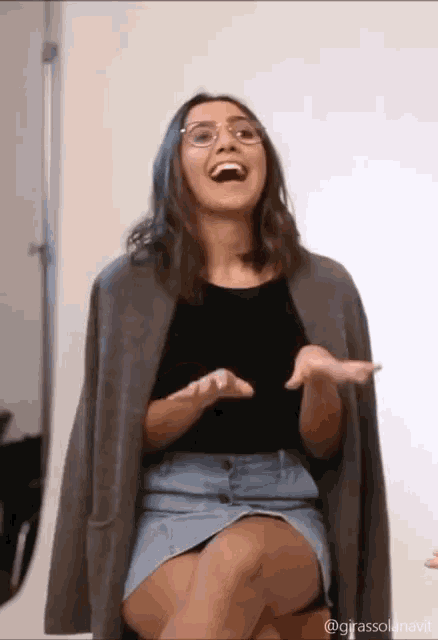 a woman wearing glasses and a denim skirt laughs