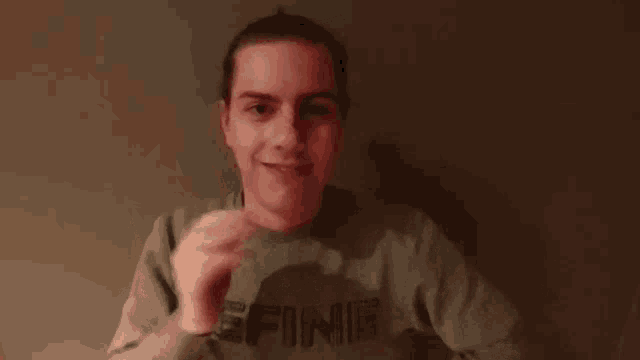 a young man wearing a sweater with the word define on it is smiling and waving his hand .