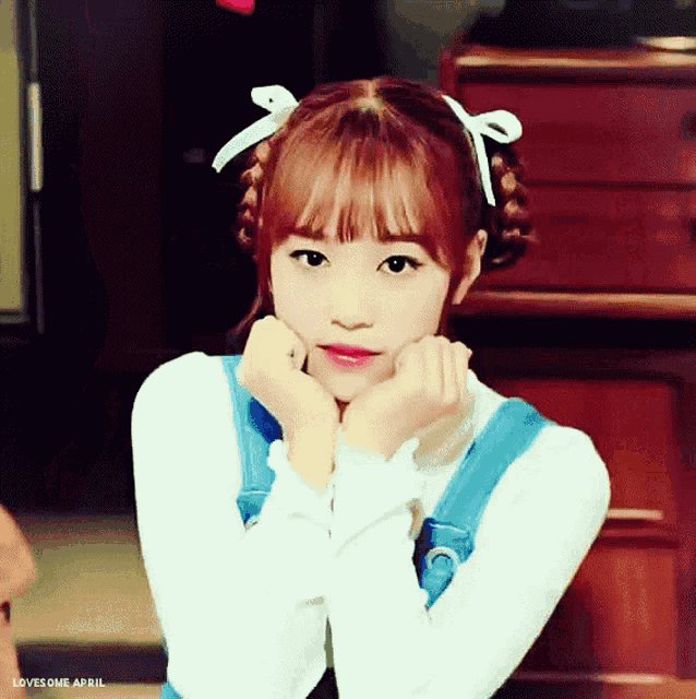 a girl with pigtails and a bow in her hair has her hands on her chin