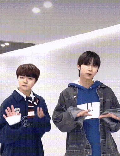 two young men are standing next to each other in a room . one of the men is wearing a blue hoodie .
