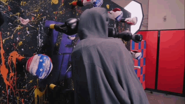 a person in a hooded cape is standing in front of a wall with boxing gloves on it