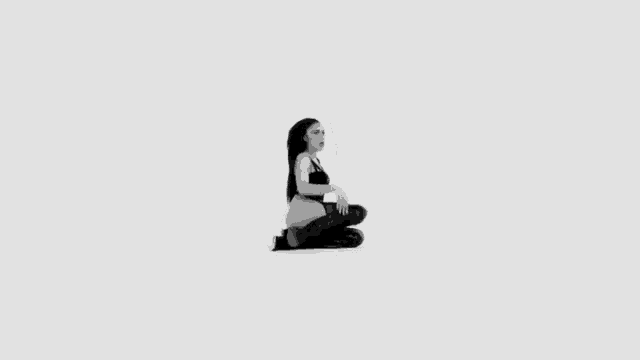 a black and white photo of a woman kneeling on the floor wearing thigh high boots .