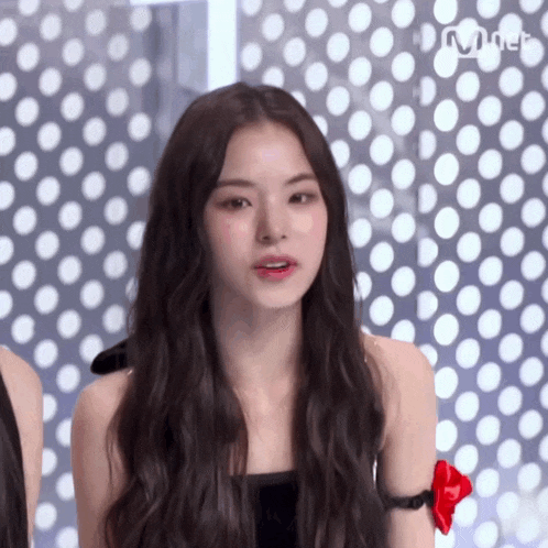 a woman with long hair is standing in front of a polka dot wall and the word mnet is on the bottom right