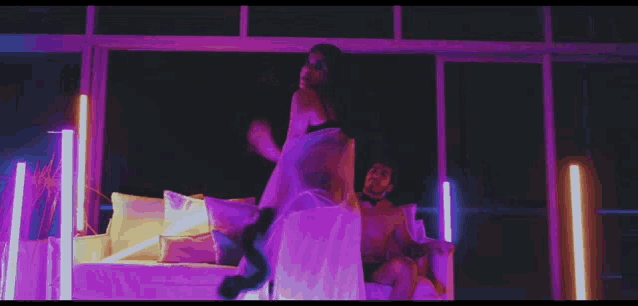 a man and a woman are sitting on a couch in a room with purple lights .