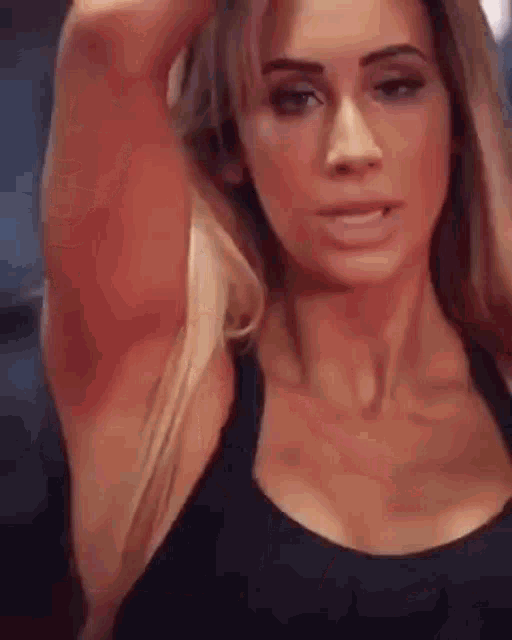 a close up of a woman in a black tank top holding her arm up .