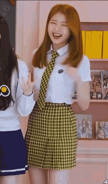 a girl in a school uniform and tie is laughing while standing next to another girl in a blue skirt .