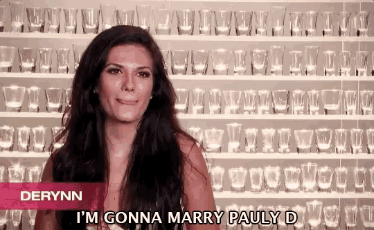 a woman is standing in front of a wall of shot glasses and says derynn i 'm gonna marry pauly d.