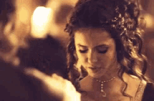 a woman wearing a tiara and a necklace is looking down at something .
