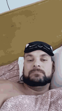 a man with a beard is laying on a bed with a black mask on his face