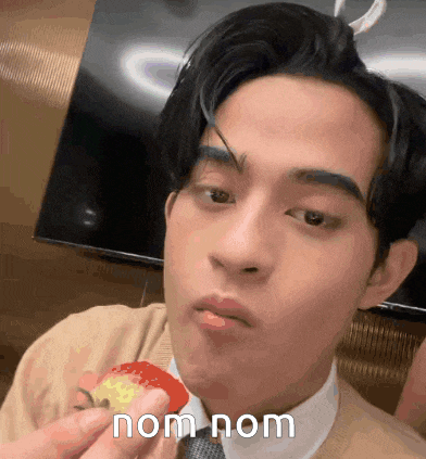 a man in a suit and tie is eating a piece of food with the words nom nom written on his face .