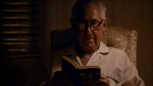 a man wearing glasses is reading a book in a dark room