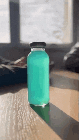 a bottle of blue liquid sits on a wooden table .