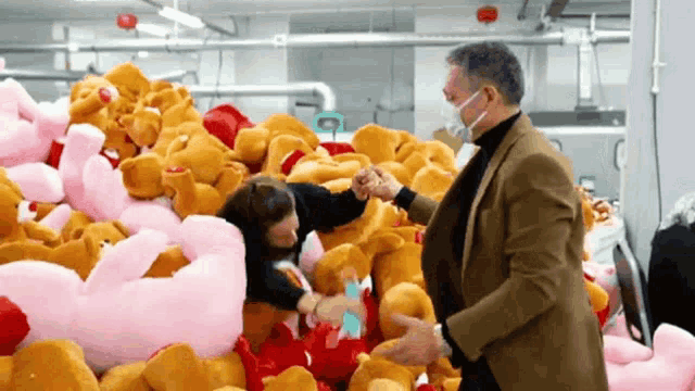 a man wearing a mask shakes hands with a woman surrounded by stuffed animals