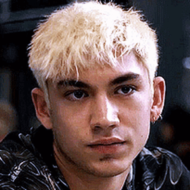 a young man with blonde hair is wearing a black jacket and earrings .