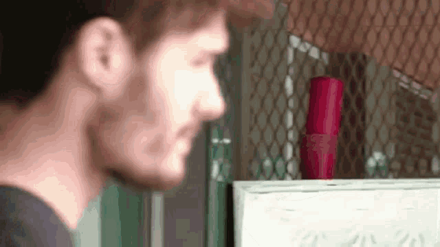 a man is standing in front of a fence and looking at a red bottle .