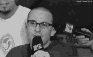a man wearing glasses is speaking into a microphone .