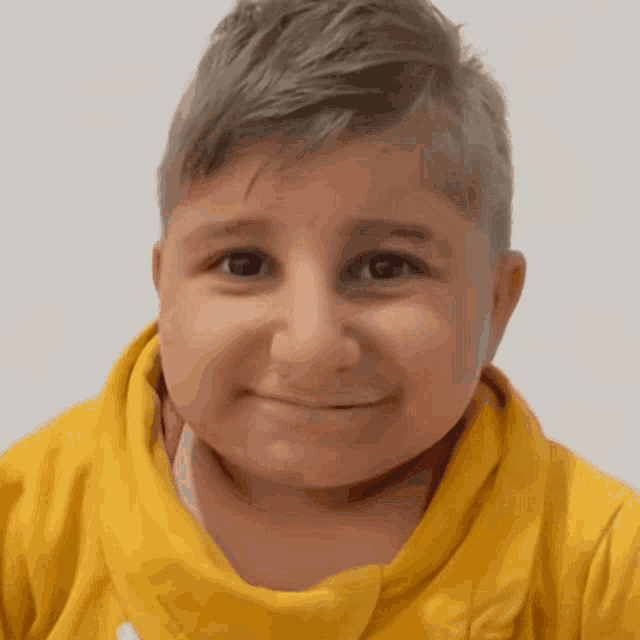 a young boy wearing a yellow sweatshirt smiles at the camera