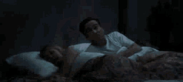 a man and a woman are laying on a bed and talking to each other . the woman is pregnant .