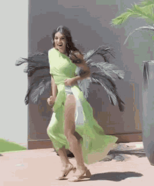 a woman in a green dress is dancing in front of a plant .