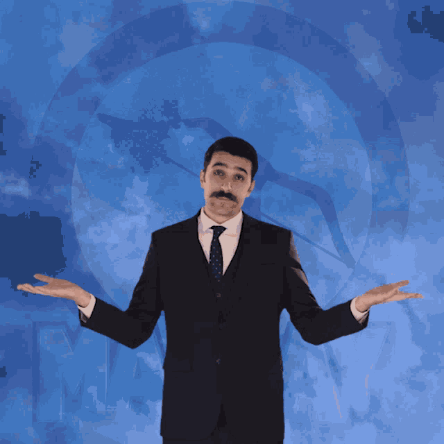 a man in a suit and tie stands in front of a blue sky with the letter m visible